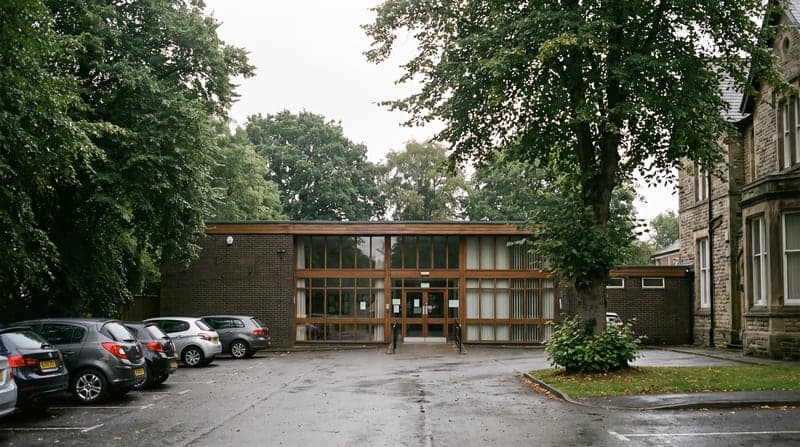 A single-storey community hall in a leafy residential street, with a larger period building alongside