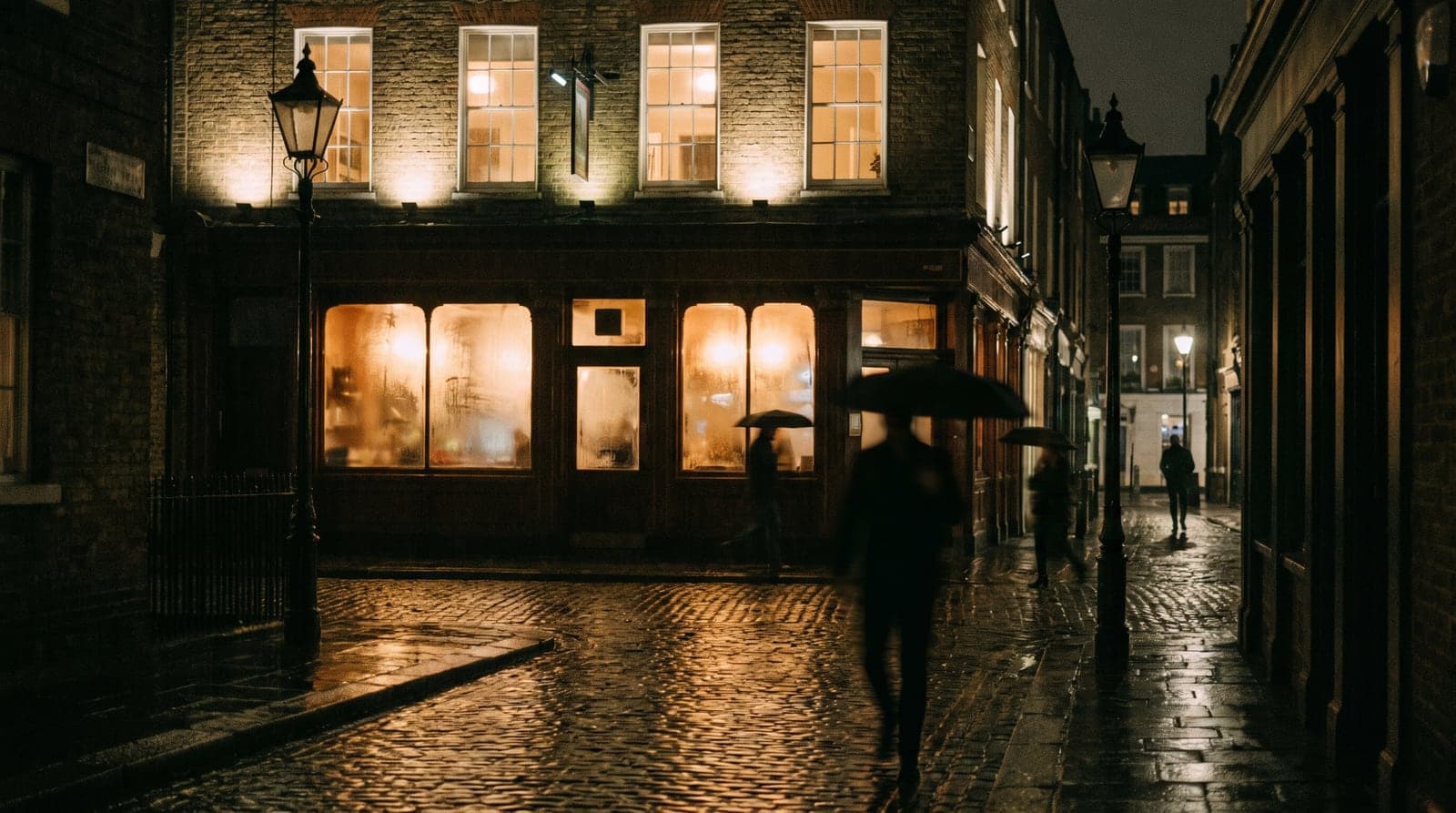 A city-centre street at night, light from a bar frontage falling on wet pavement below residential windows