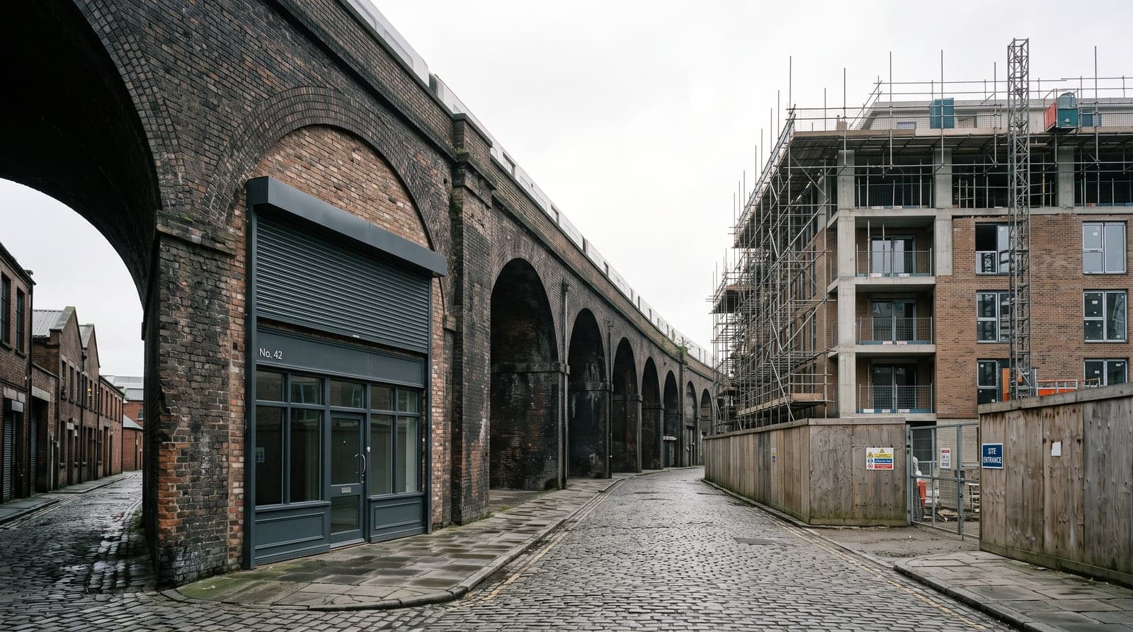 A brick railway arch fitted out as a commercial unit, a new apartment block rising behind hoardings across the street