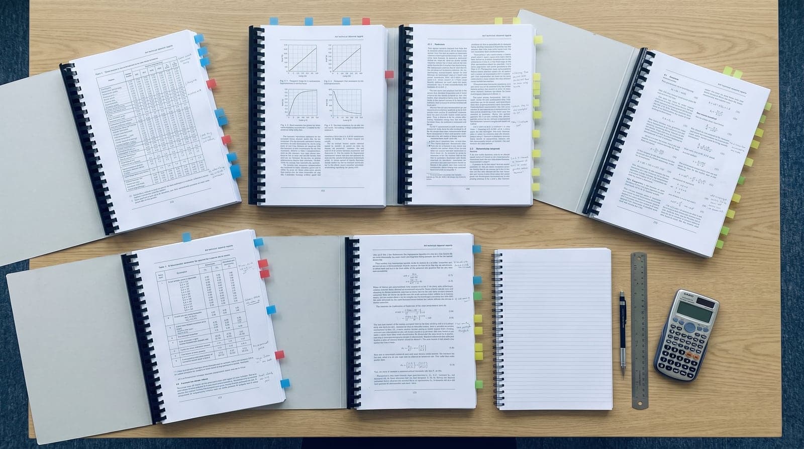 Technical standards open across a desk, tabbed and annotated, beside a rule and a calculator