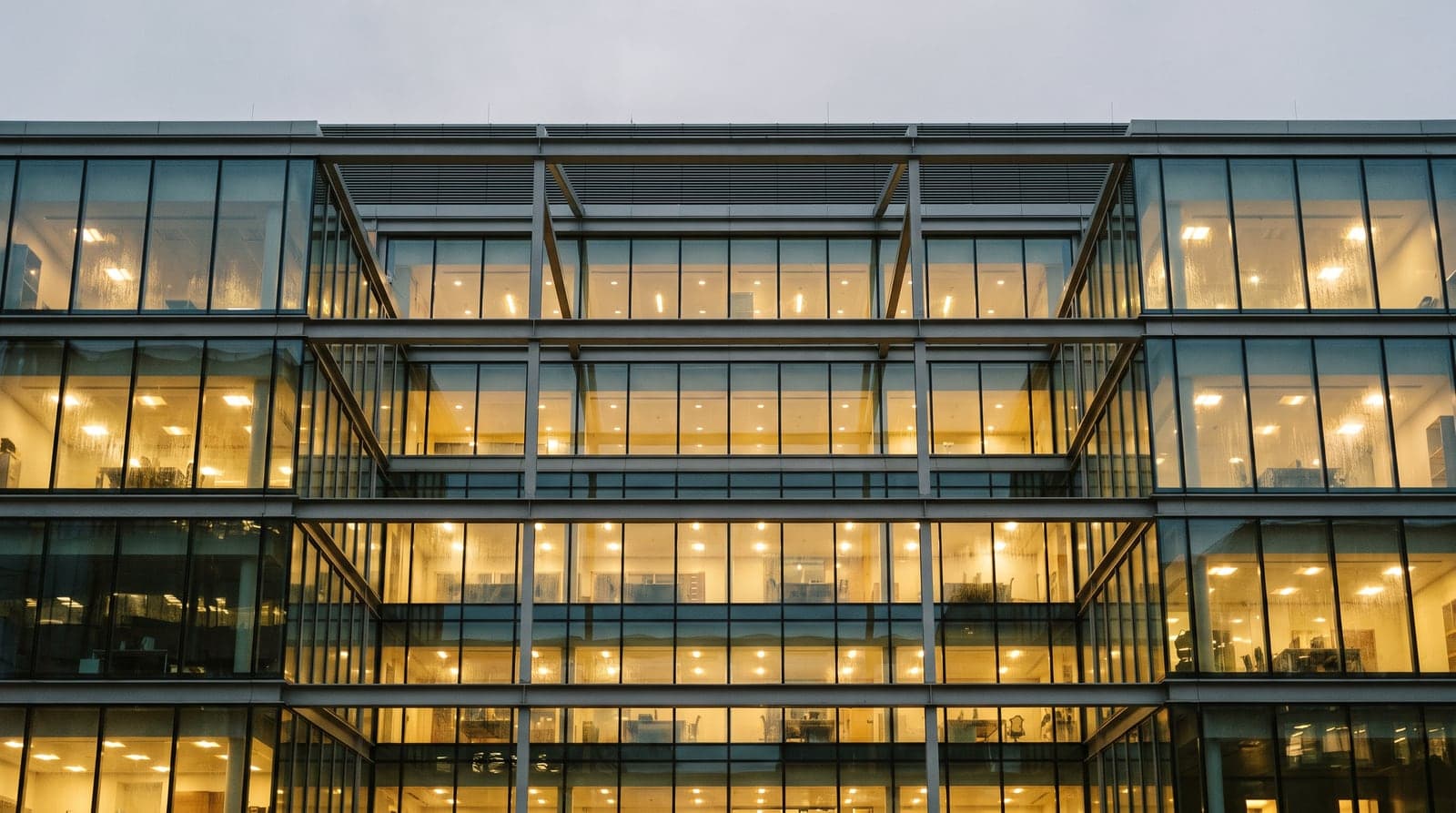 The upper floors of a modern office building at dusk, warm light behind the glazing