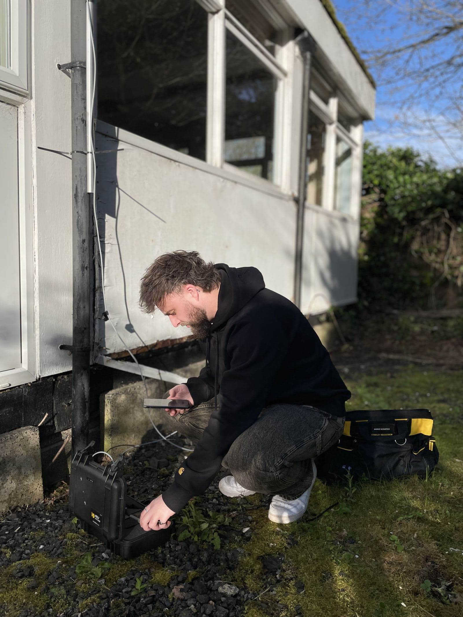 A Murray Acoustics engineer setting up monitoring equipment against a building façade