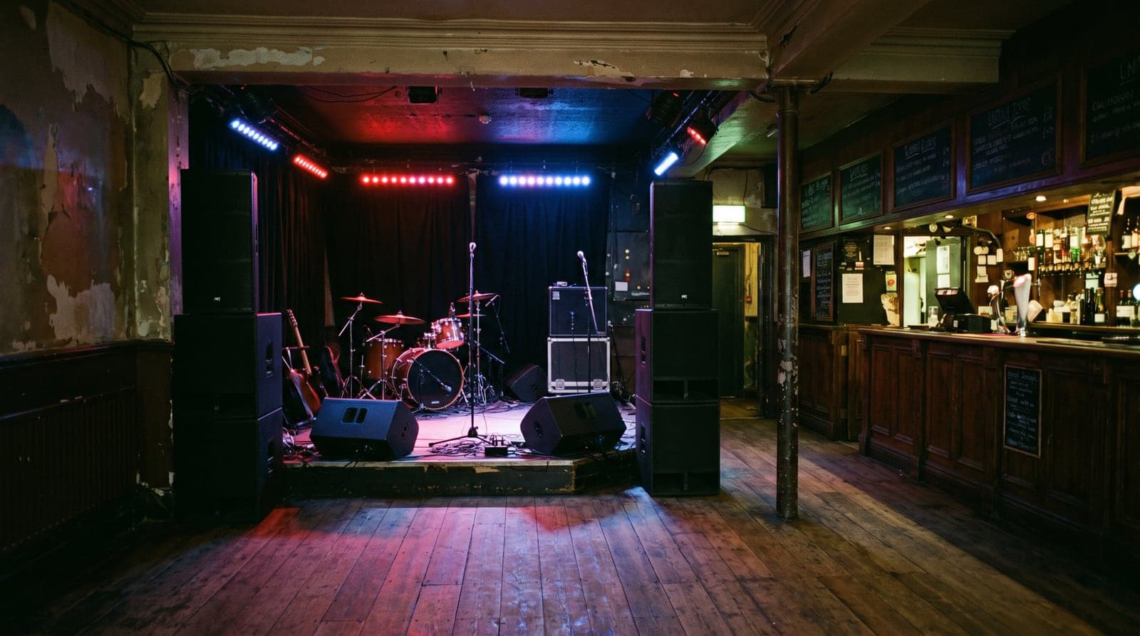 Bar frontage at night with open doors, a speaker stack inside and people on the pavement