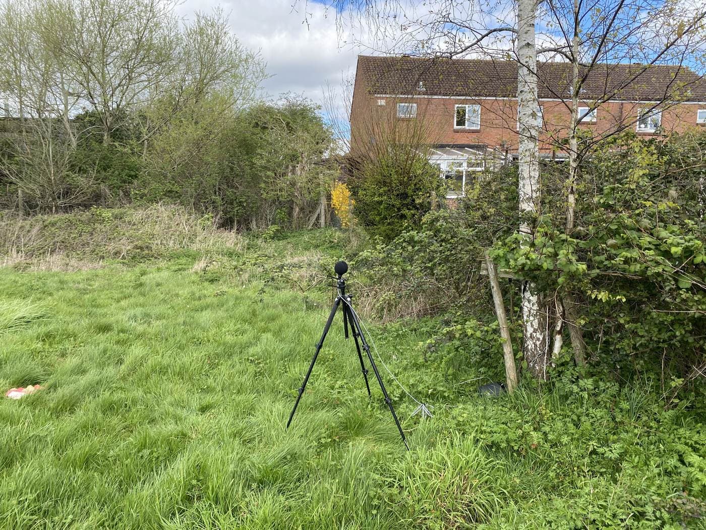 A sound level meter on a tripod in a field beside a residential development site
