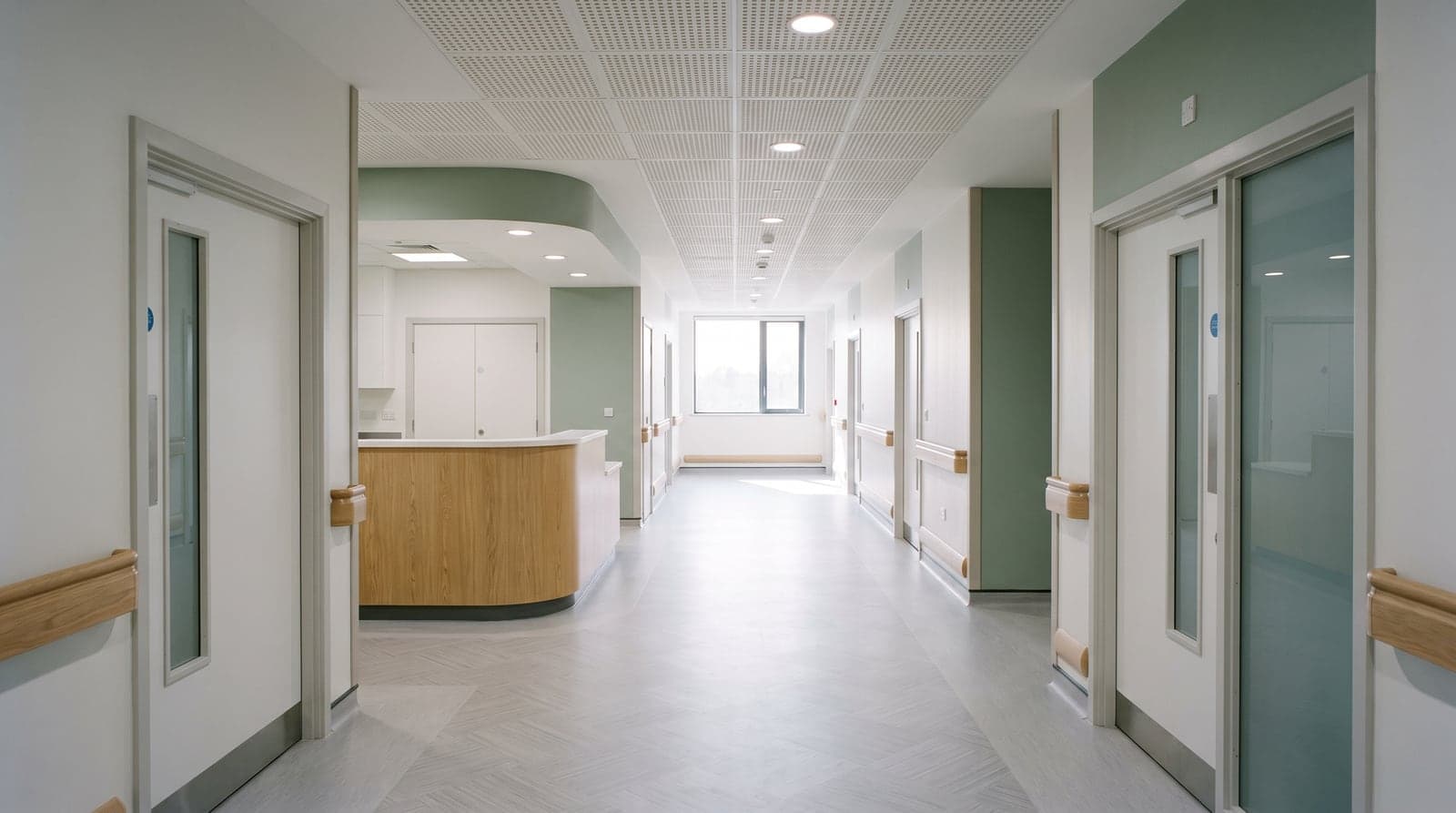 A hospital ward corridor with a nurses' station and an acoustic ceiling