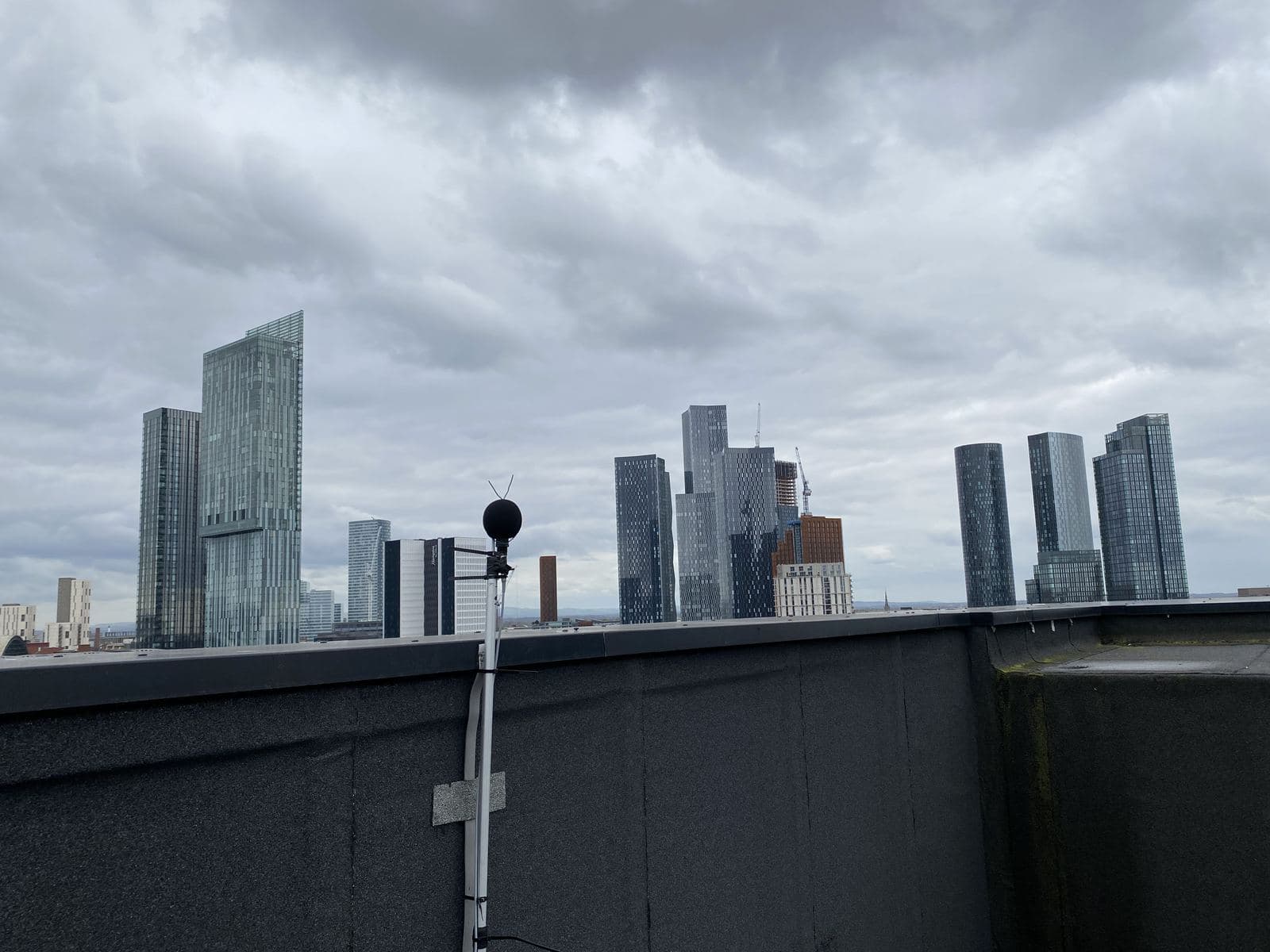 A sound level meter set up on a rooftop beside mechanical plant
