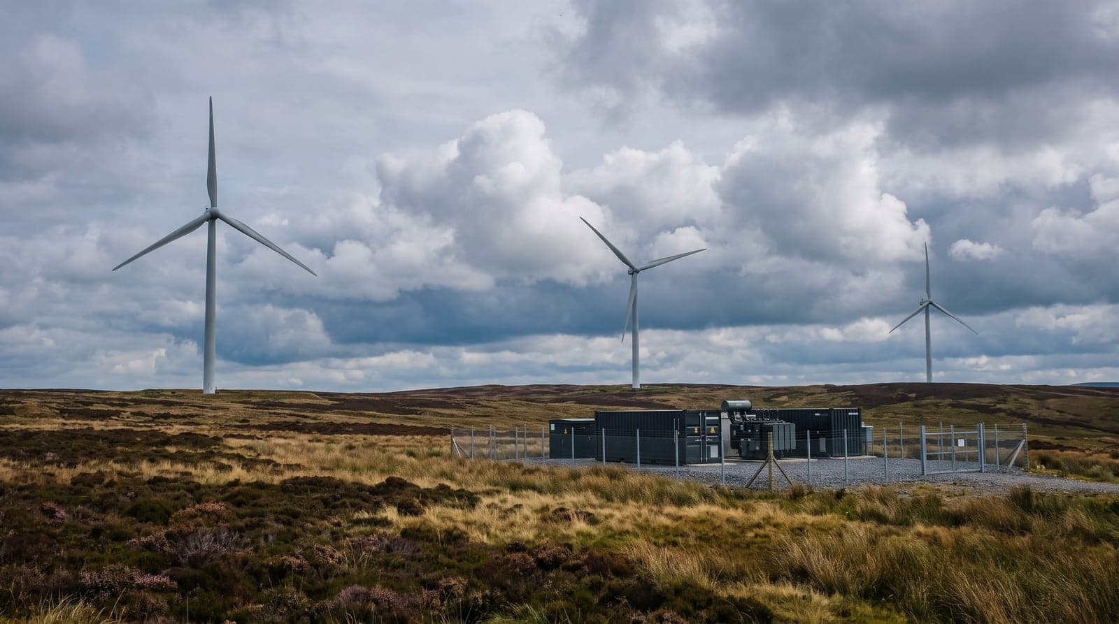 Battery storage containers alongside solar panels and a wind turbine